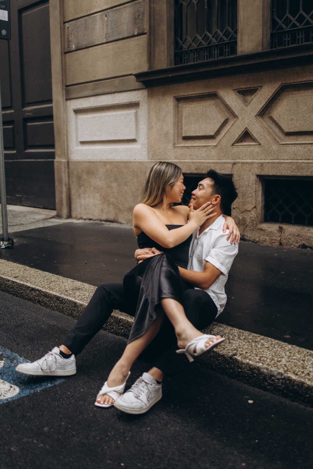 Couple sitting close on a curb, foreheads nearly touching, during a couple photoshoot in Milan