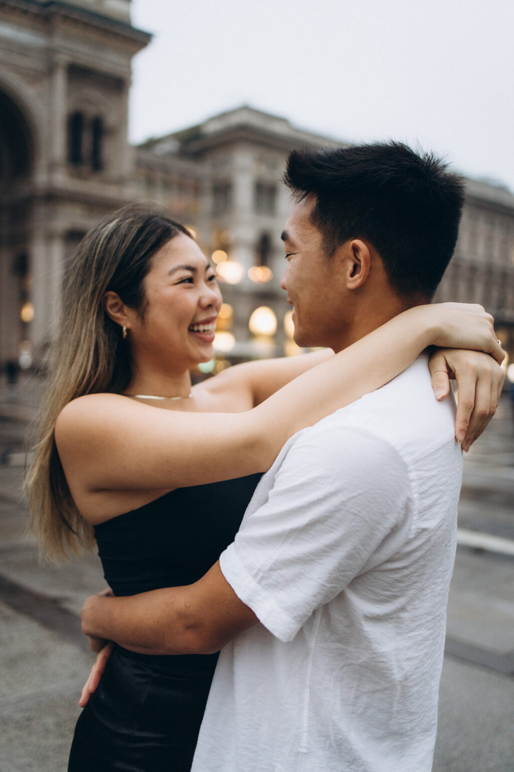 Couple Photo in Milan - A couple laughing in a warm embrace in Piazza del Duomo, with the Galleria Vittorio Emanuele II glowing softly behind them