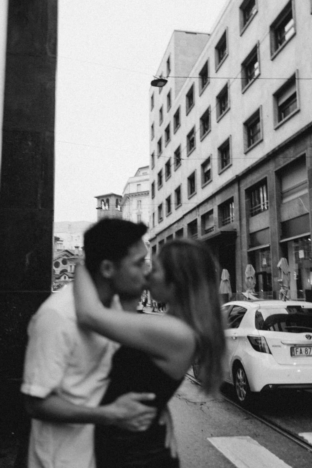 A black and white shot of a couple kissing on a city street, their embrace softly blurred with motion