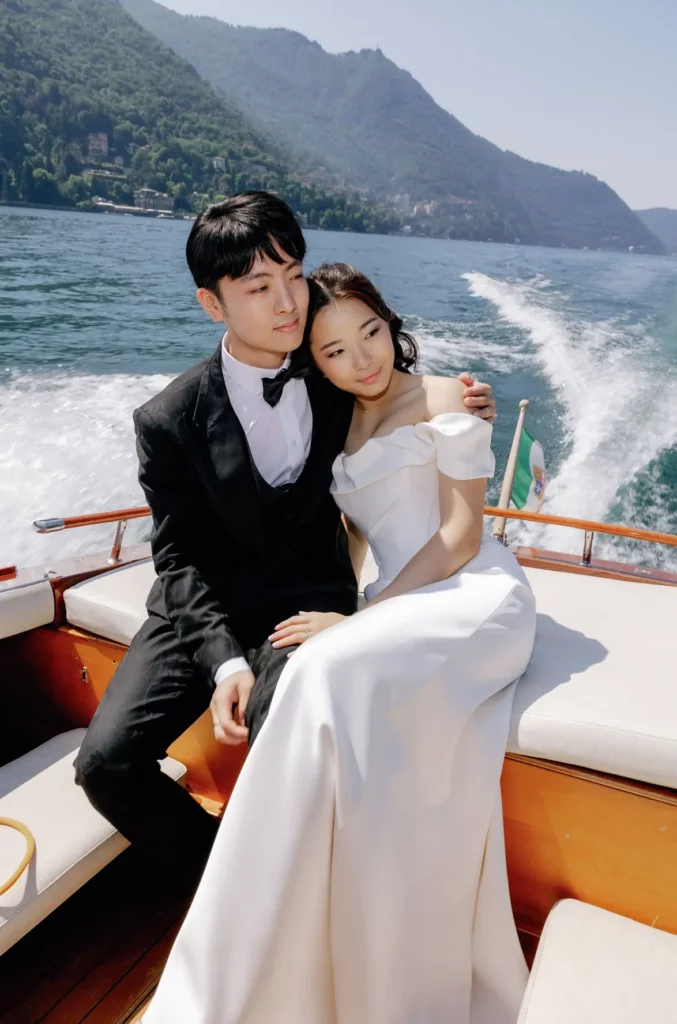 Bride leaning on the groom’s shoulder in the stern of a wooden boat on Lake Como