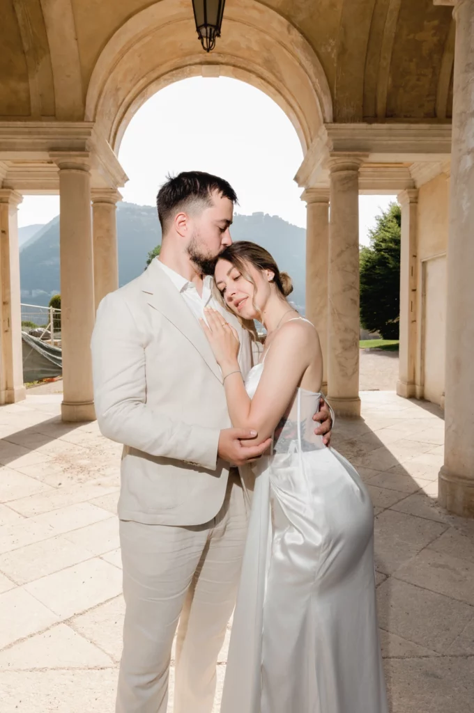 Groom kissing his bride beneath the colonnade of Villa Olmo, Como