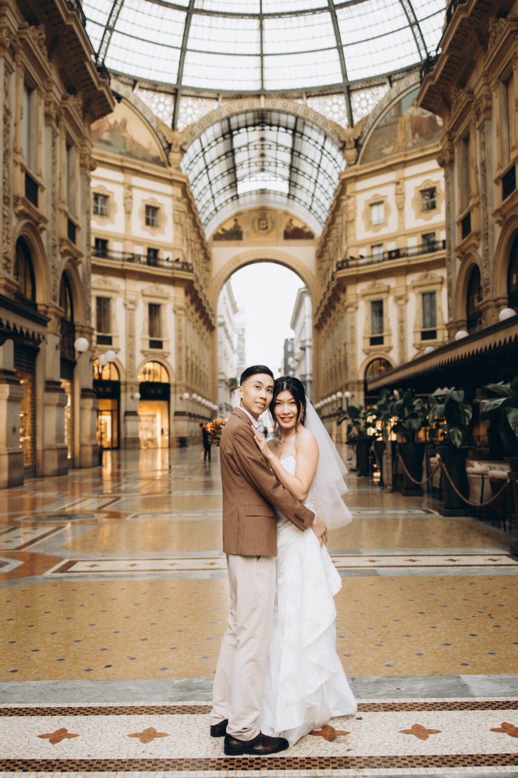 Bride-to-be and groom-to-be embracing and smiling at the camera under the glass dome of the Galleria Vittorio Emanuele II in Milan