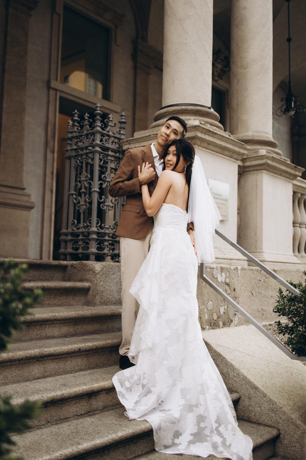 Bride-to-be resting against her groom-to-be as they embrace on the steps of the Palazzo Giureconsulti on Piazza dei Mercanti in Milan