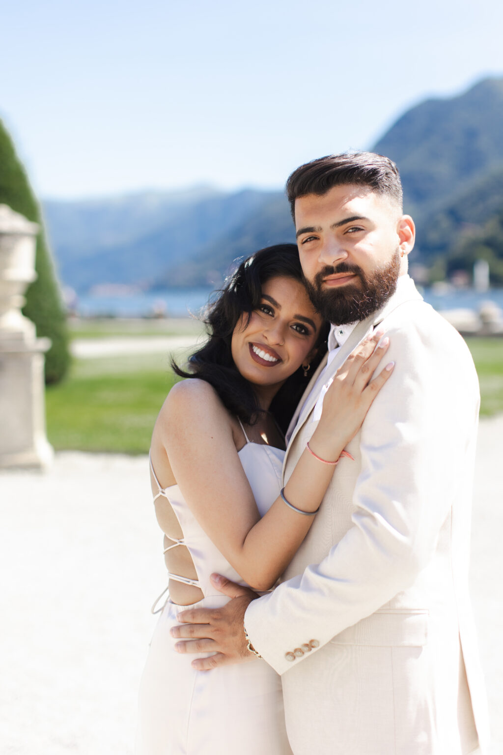 Couple pressing cheek to cheek and smiling warmly at the camera in a villa garden on Lake Como