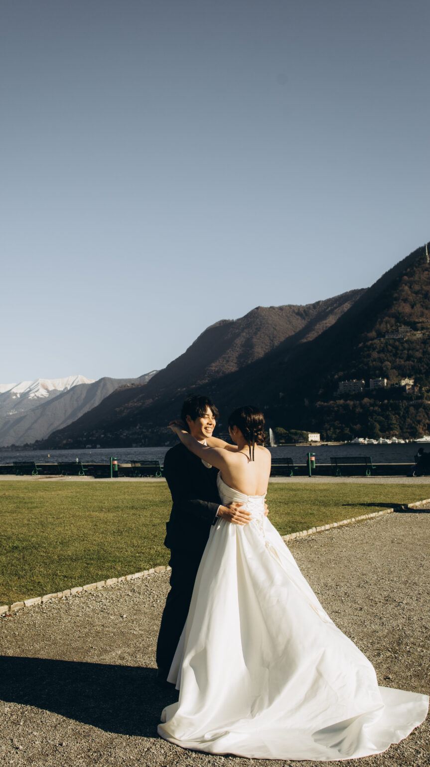 Bride and groom embracing on the Como lakefront lawn with the lake, mountains and a fountain jet behind them