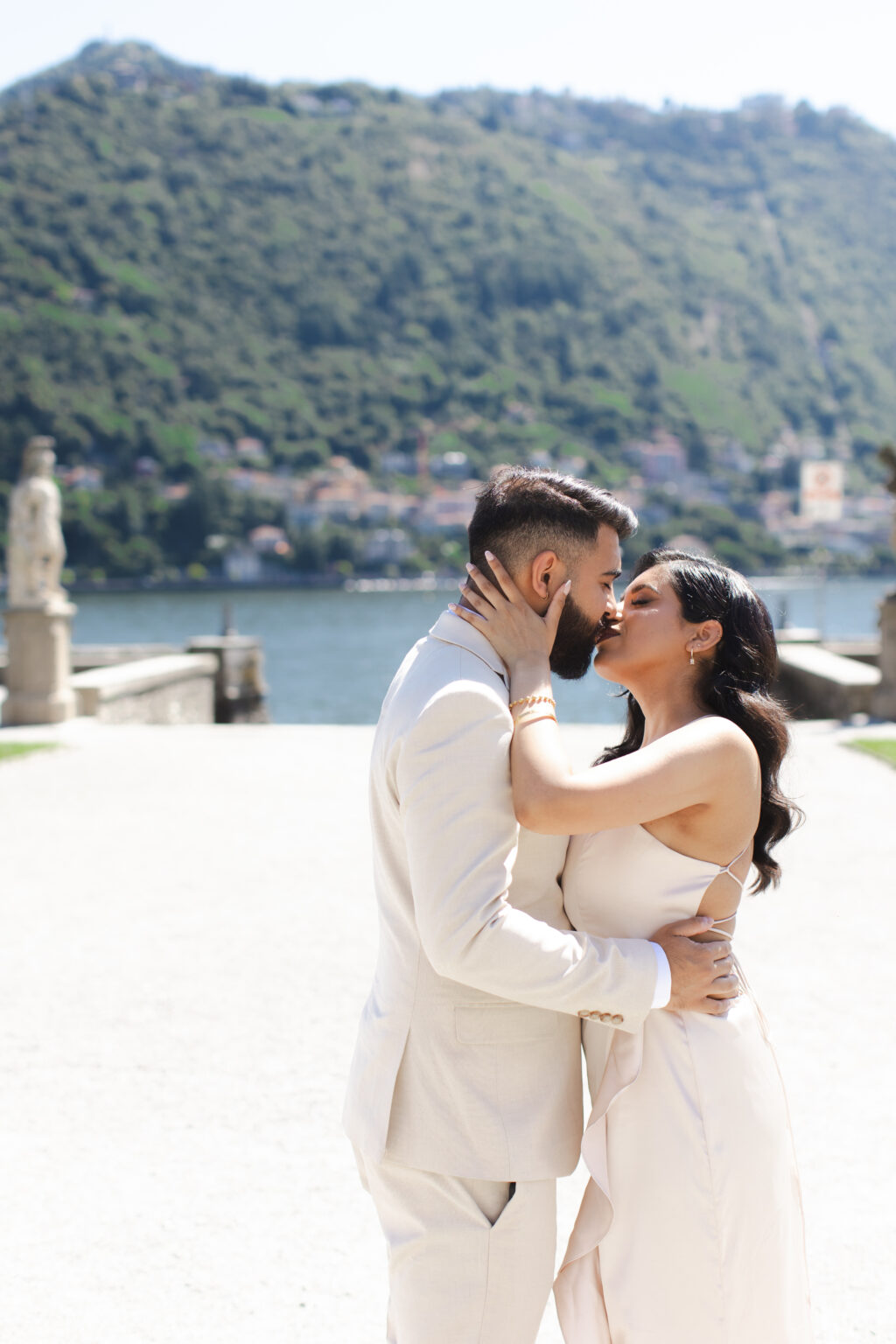 Couple sharing a kiss on a villa terrace with the balustrade, lake and town of Como softly blurred behind them on Lake Como