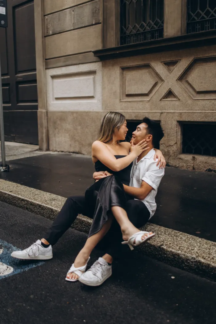 Couple sitting close on a curb, foreheads nearly touching, during a couple photoshoot in Milan