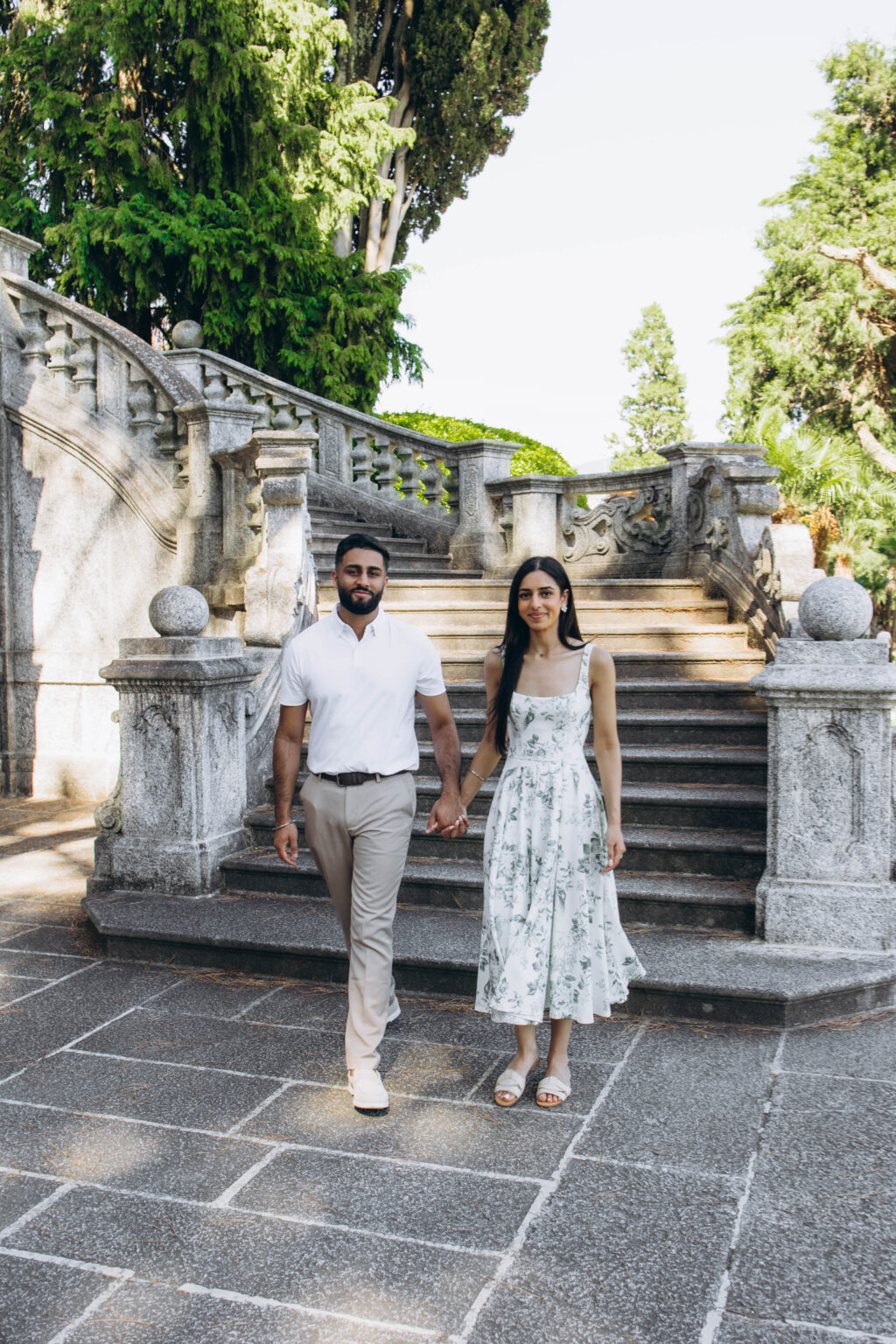 Couple in a white polo and a green floral midi dress walking hand in hand from the staircase of Parco Teresio Olivelli in Tremezzo