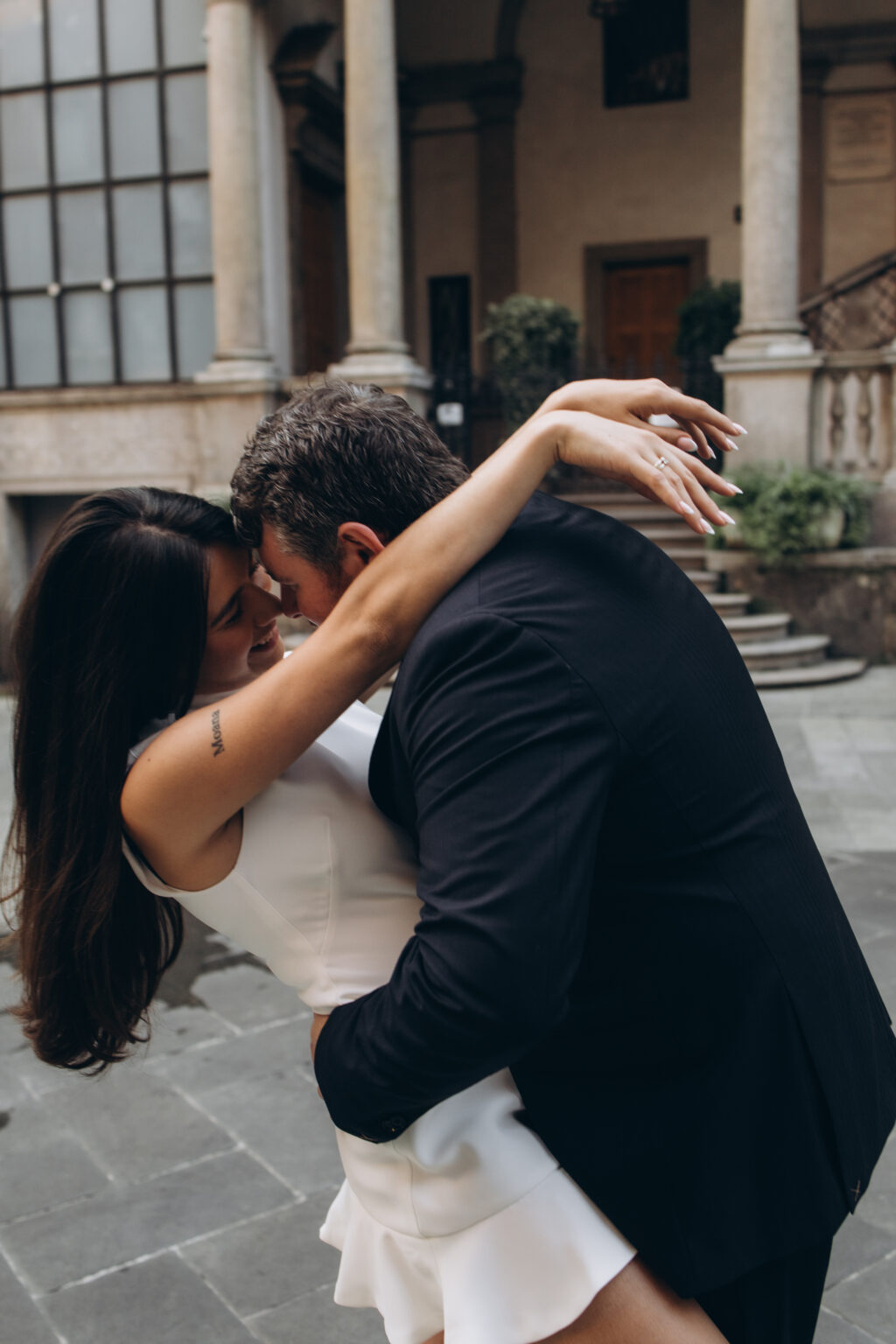 Man leaning his fiancee back into a close embrace forehead to forehead in a columned courtyard on Piazza dei Mercanti in Milan