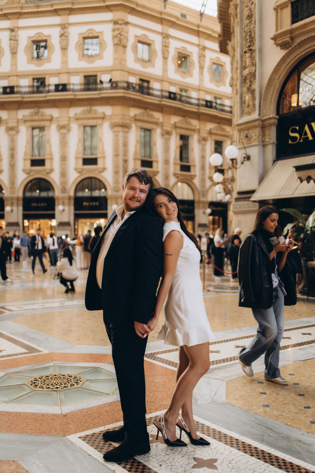 Engaged couple standing back to back and holding hands on the mosaic floor of the Galleria Vittorio Emanuele II in Milan