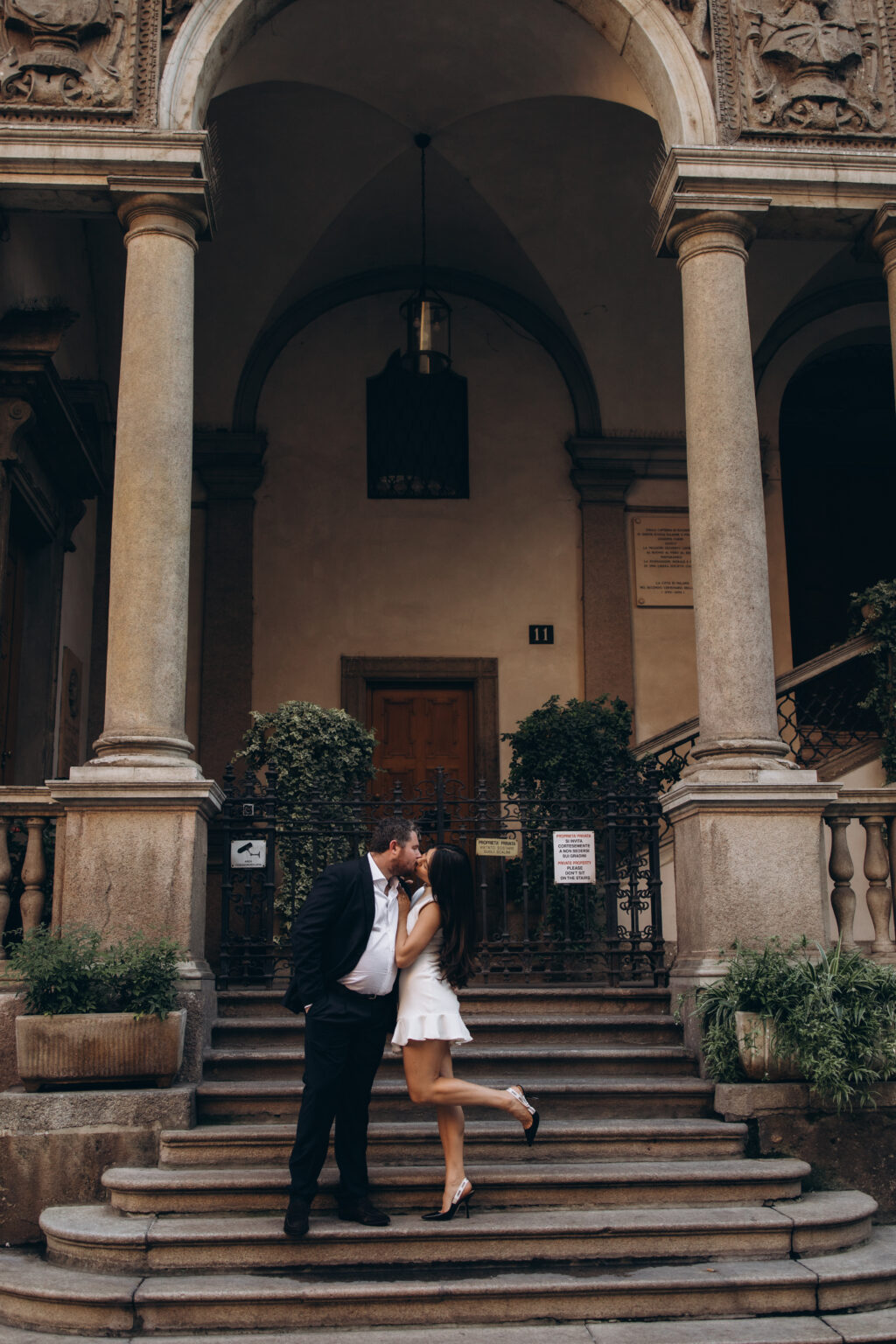 Newly engaged couple kissing on the stone steps of a historic private palazzo courtyard with columns in central Milan