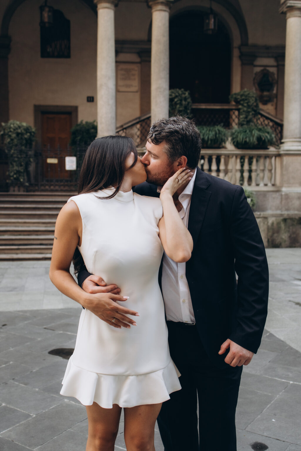 Newly engaged couple kissing on the steps of a historic columned portico on Piazza dei Mercanti in central Milan