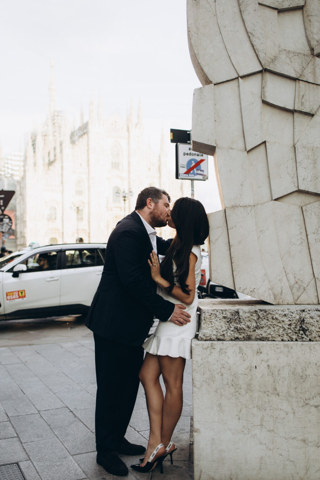Newly engaged couple kissing on Piazza del Duomo with the Duomo cathedral rising behind them in Milan