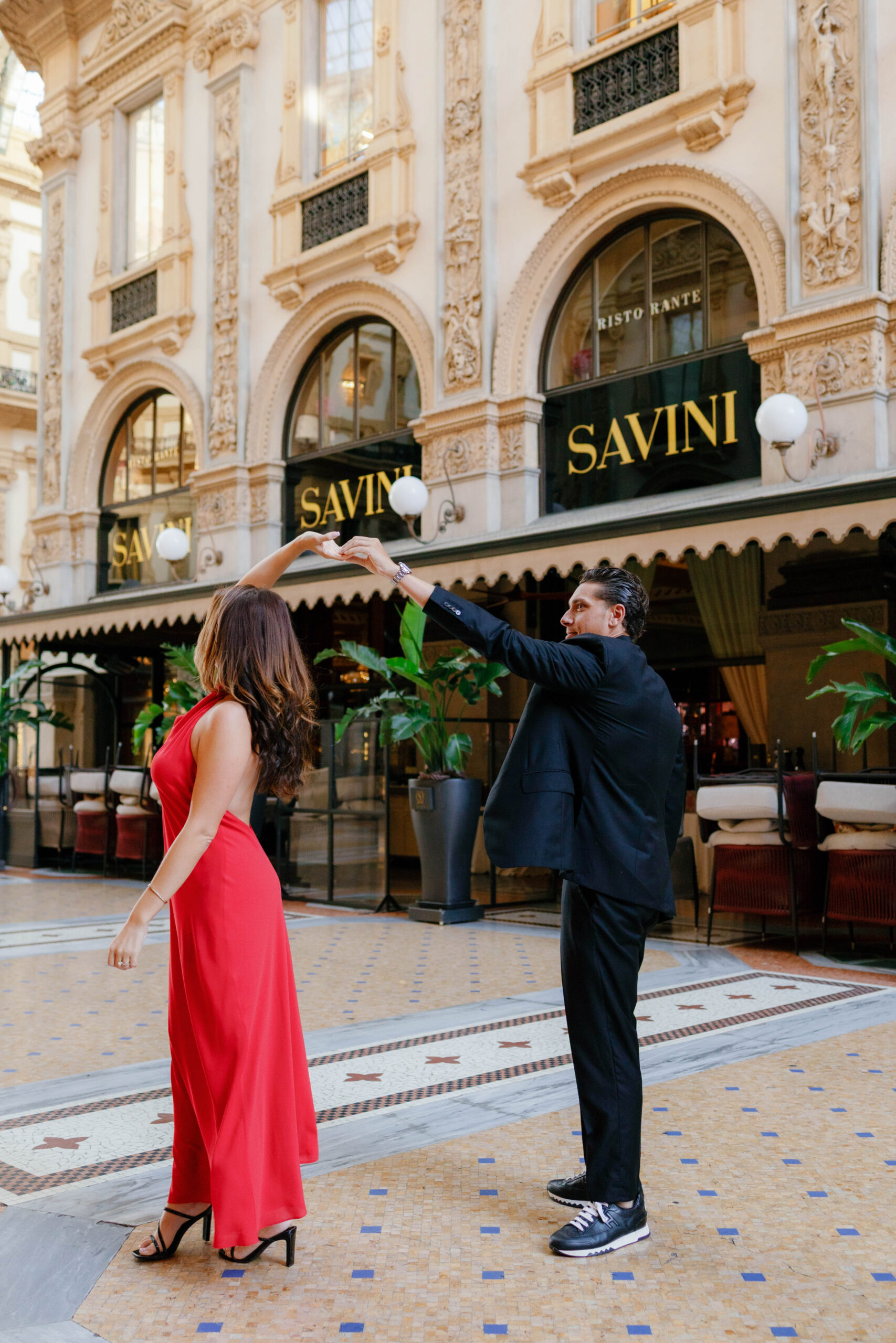 A man twirls his partner in a red dress under the arcades of Galleria Vittorio Emanuele II in Milan