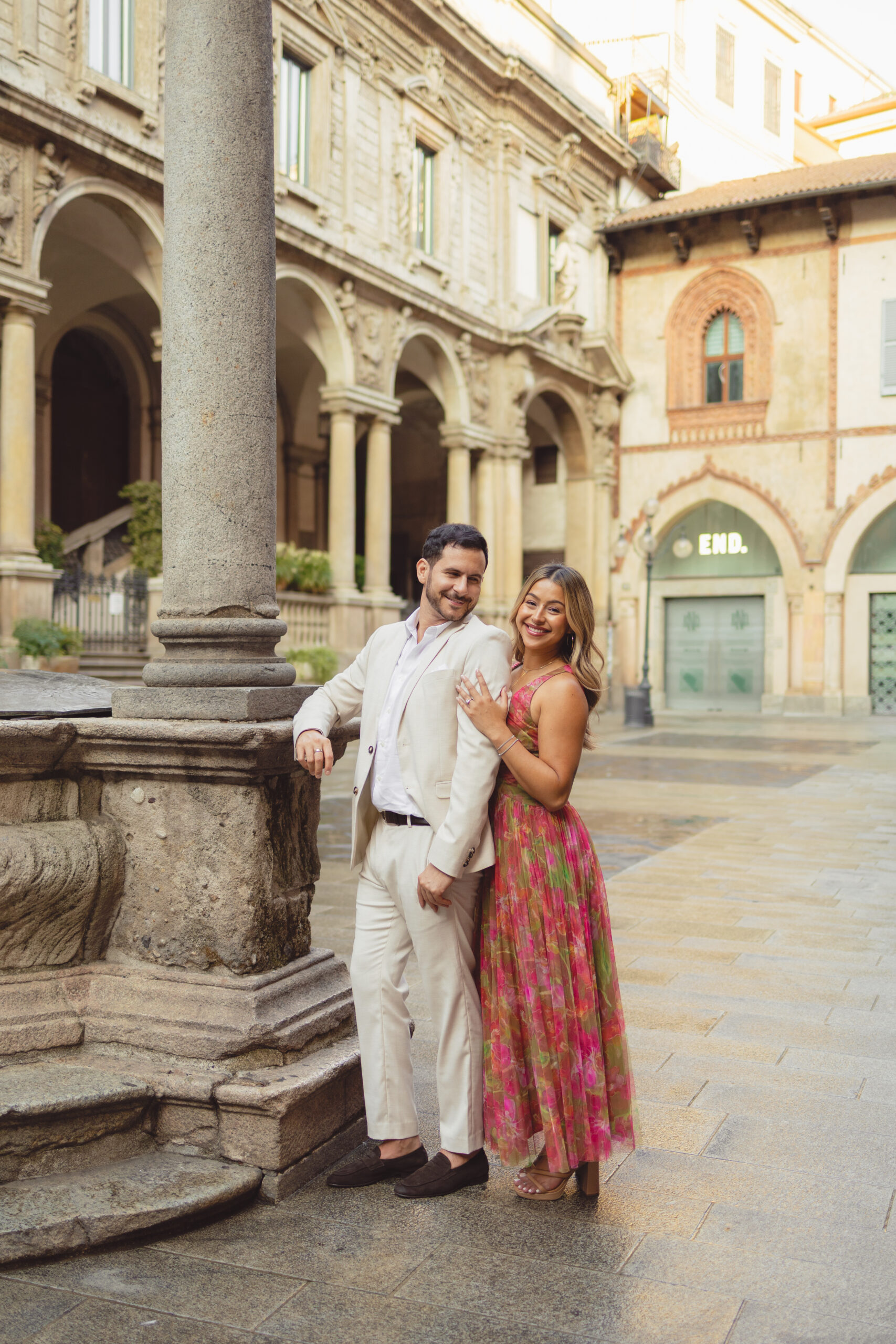 A newly engaged couple poses for a portrait in the historic Piazza Mercanti, one of Milan's quiet medieval squares just steps from the Duomo. Photographed by Julia, private proposal and engagement photographer in Milan.