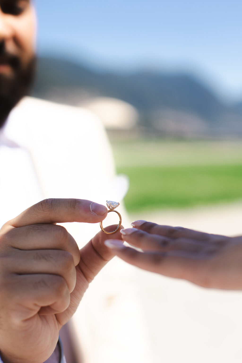 A pear-cut diamond engagement ring held up between two fingers before the proposal, the green hills above Lake Como blurred behind it.