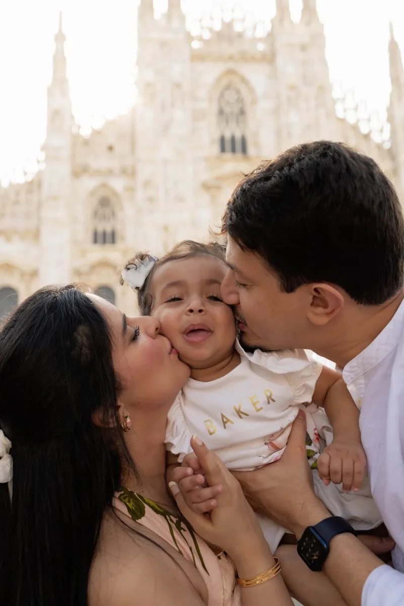 Parents kissing their laughing baby in front of the Duomo in Milan