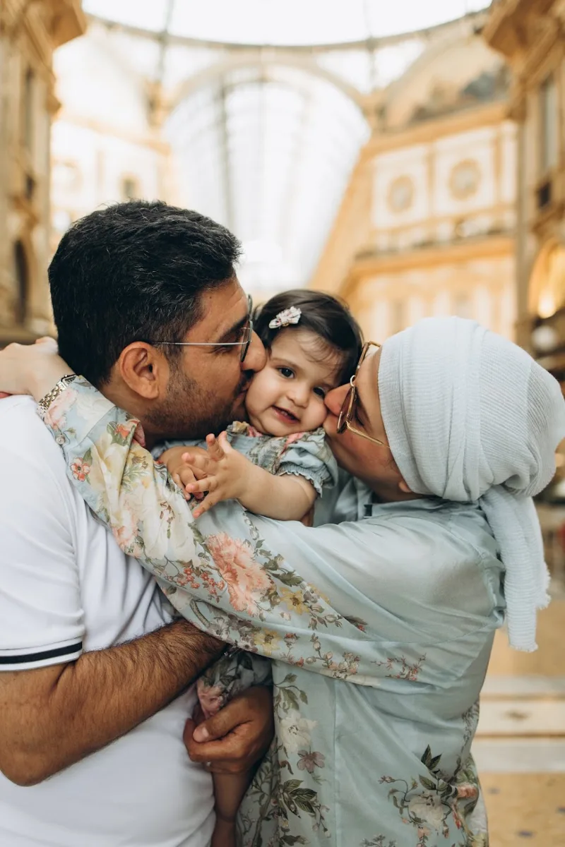 Parents kissing their baby daughter under the glass dome of the Galleria Vittorio Emanuele II, Milan