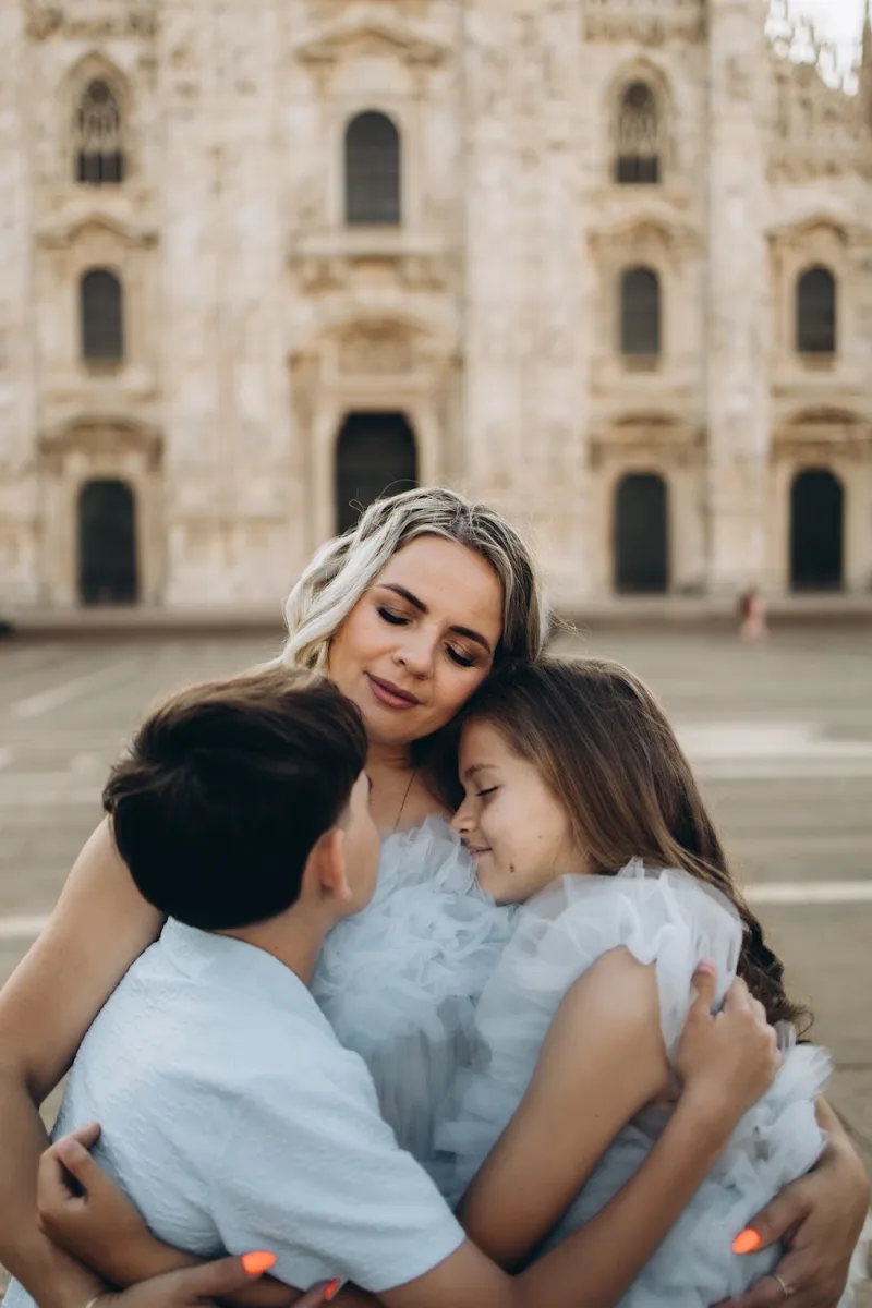 Mother in a tulle dress hugging her two children at the Duomo, Milan