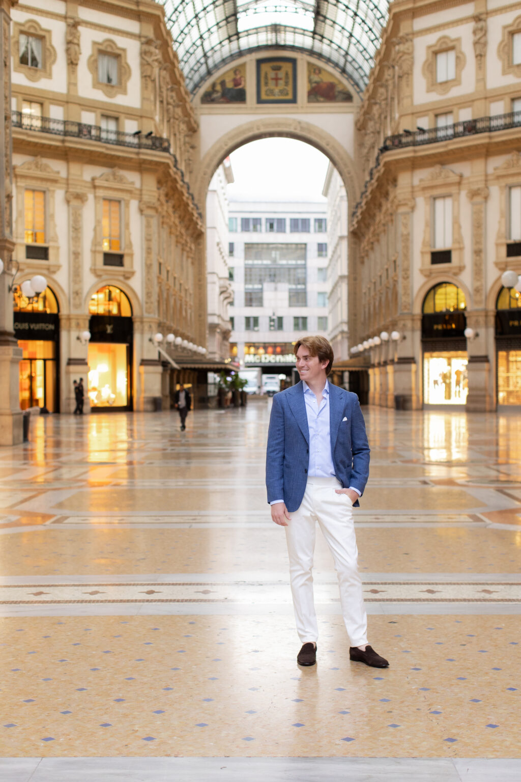 A man standing in the vast empty Galleria Vittorio Emanuele II in Milan, the glass dome and mosaic floor stretching around him.