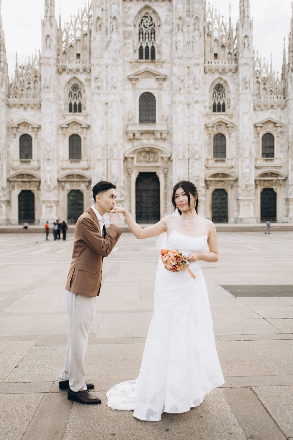 Groom-to-be kissing his bride-to-be's hand in front of the Duomo cathedral facade on Piazza del Duomo in Milan