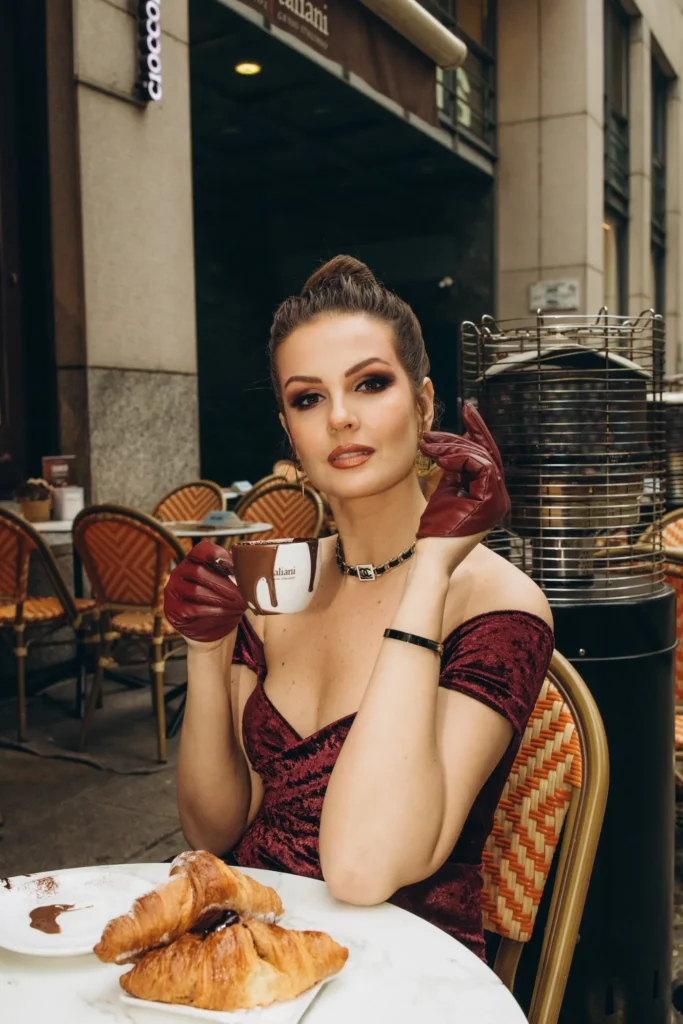 Woman in a burgundy gown and gloves at a Milan café table