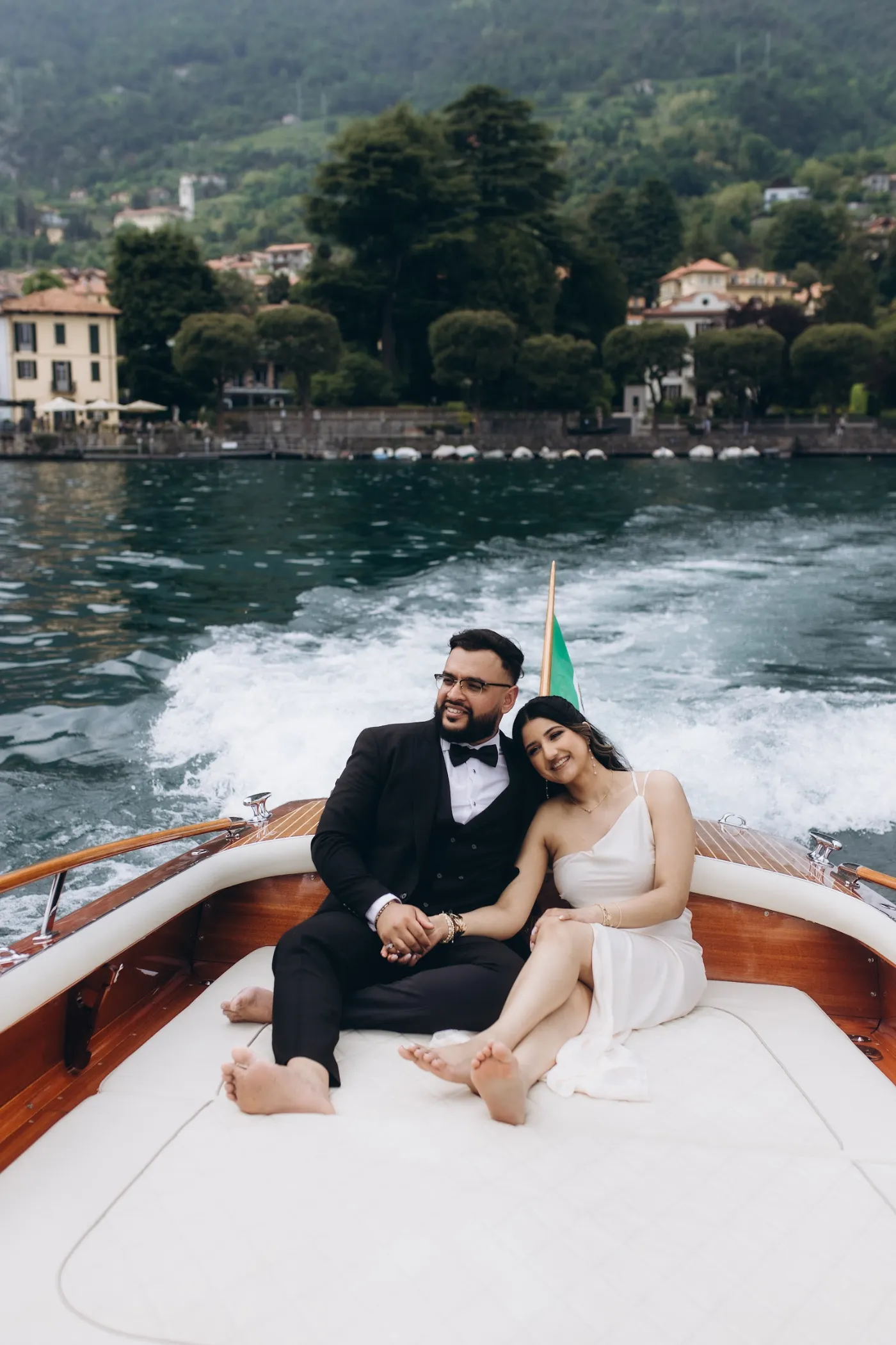 Couple on a wooden boat speeding past Villa del Balbianello, Lake Como