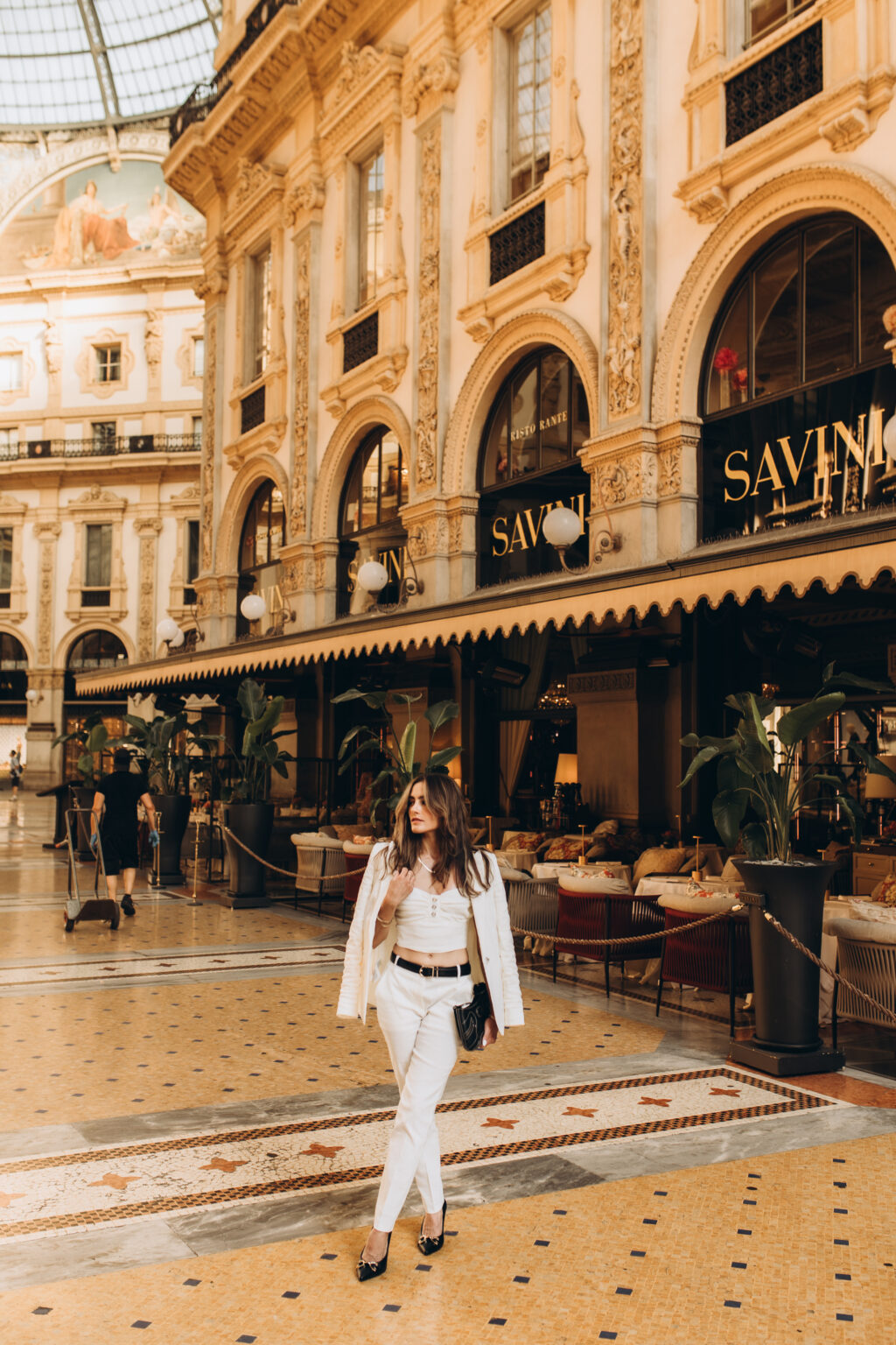 Woman in a white suit walks across the mosaic floor near the Savini restaurant in the Galleria Vittorio Emanuele II in Milan.