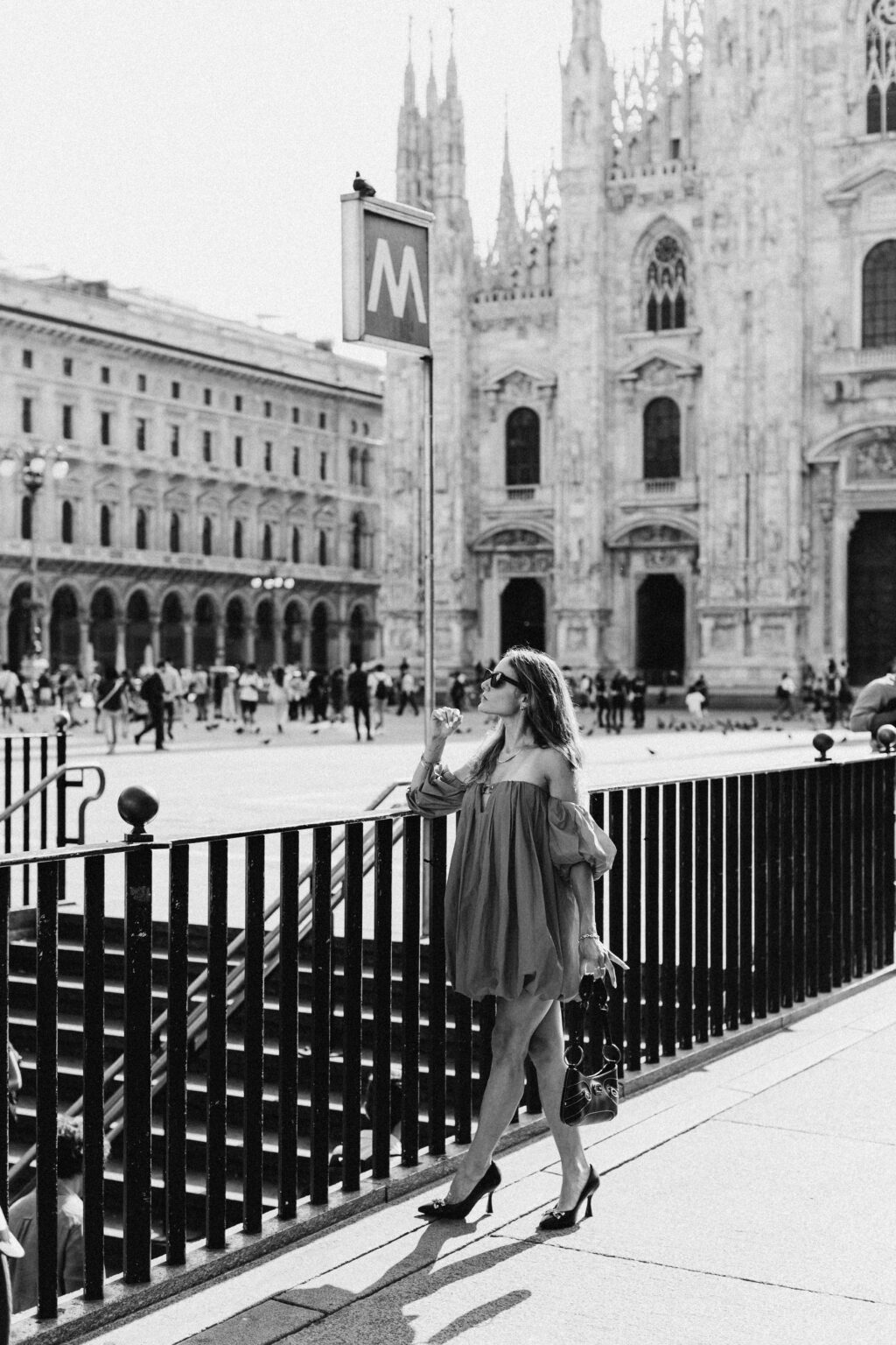 Black and white photo of a woman in a red dress by a railing with the Duomo di Milano behind her in Milan.