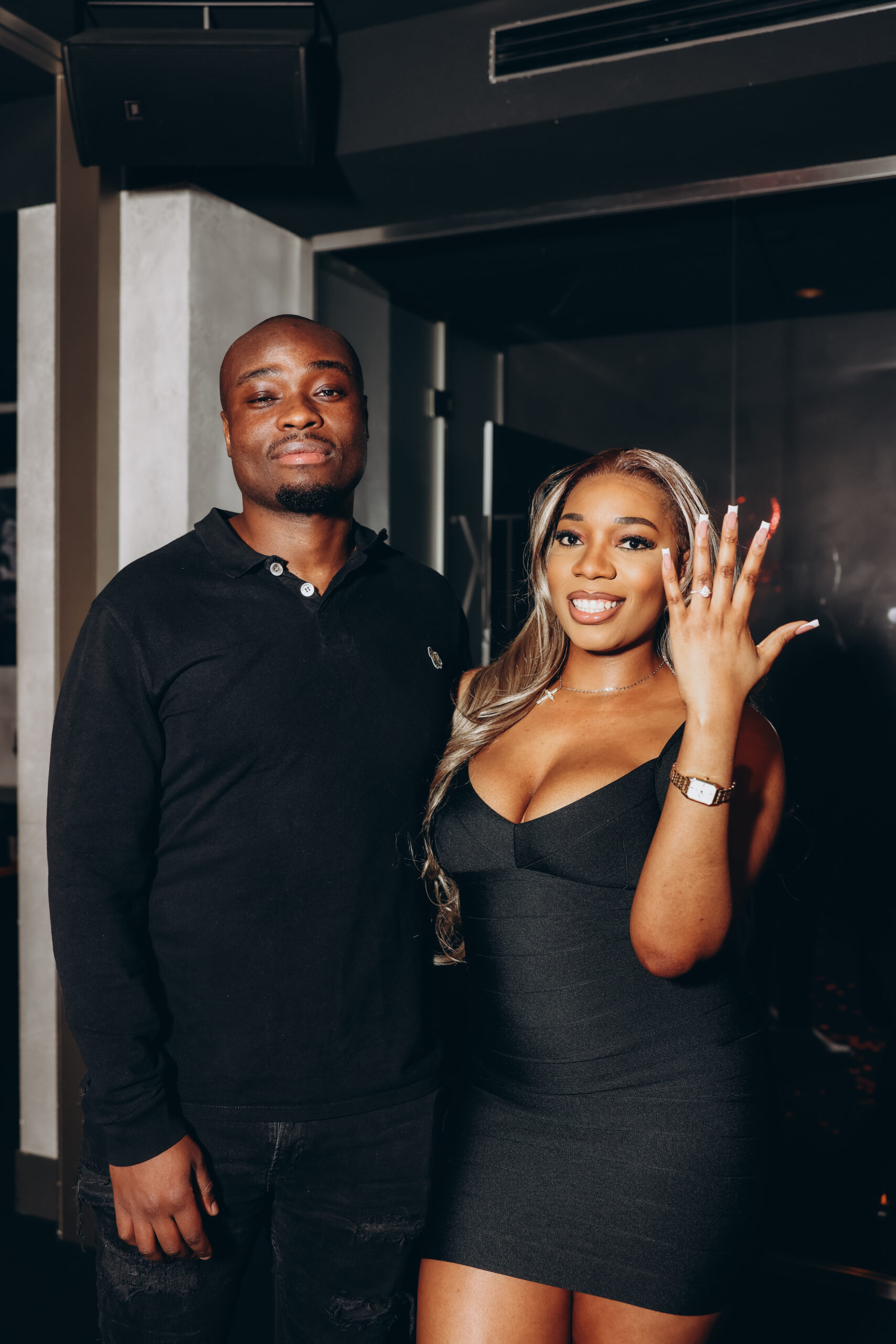A newly engaged couple smiles for a portrait as the woman shows off her engagement ring in Milan
