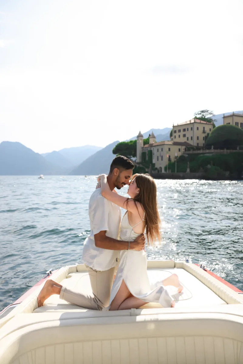 Newly engaged couple embracing on a wooden boat in front of Villa del Balbianello, Lake Como