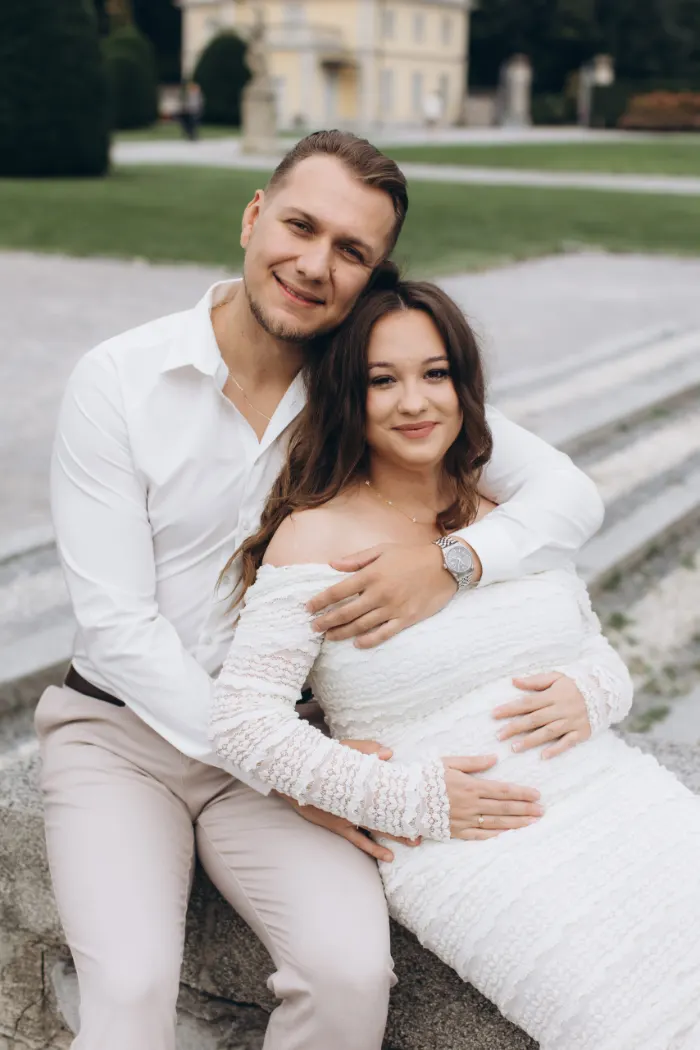 Expecting couple sitting close and smiling at Villa Olmo on Lake Como