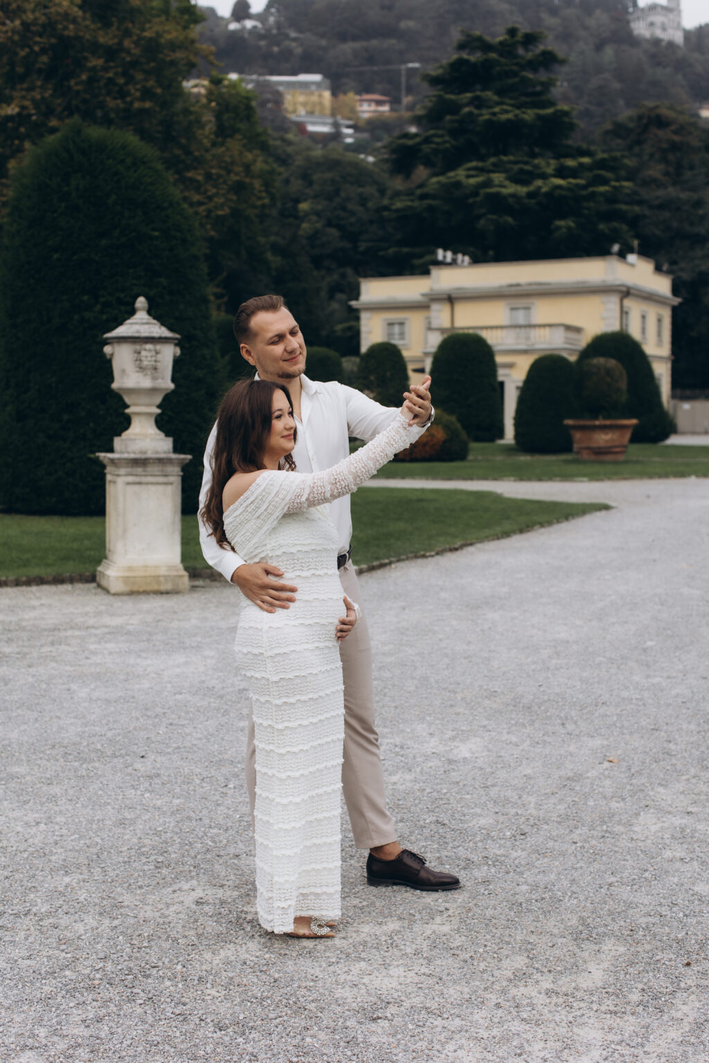 A newly engaged couple share a playful dance pose before an ochre neoclassical villa and topiary garden in the park of Villa Olmo, on Lake Como.