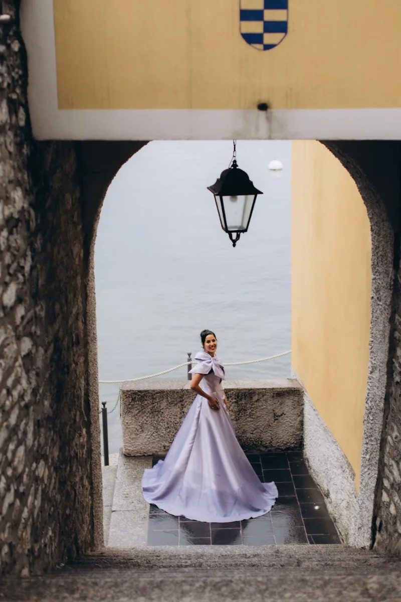 Woman in a lilac gown framed by a stone arch above the lake in Varenna