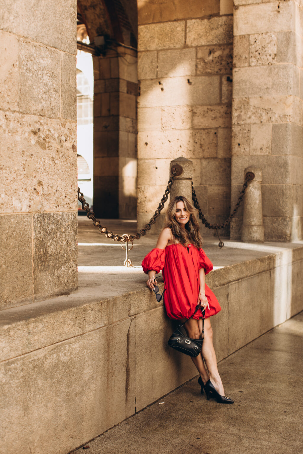 Woman in a red dress sits on the stone ledge beneath the arcades of the Palazzo della Ragione on Piazza dei Mercanti in Milan.
