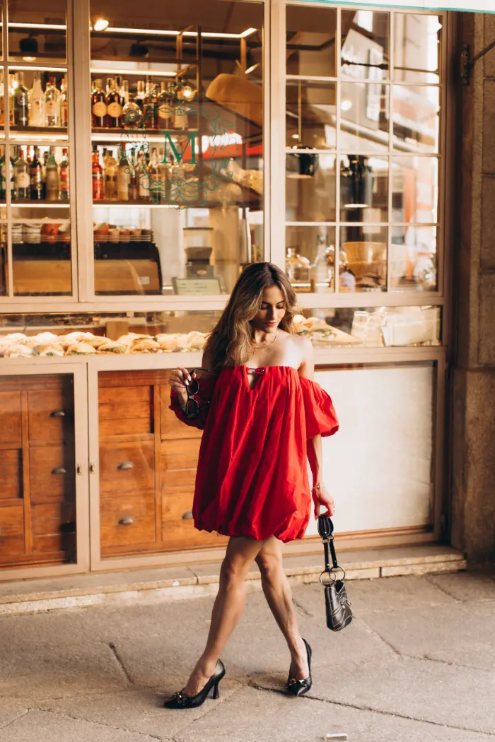Woman in a red dress walking past a historic café storefront in Milan