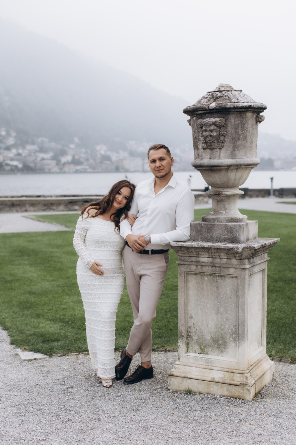 She leans against him beside a weathered stone garden urn on a pedestal in the Italian garden of Villa Olmo, the misty lake behind them, on Lake Como.