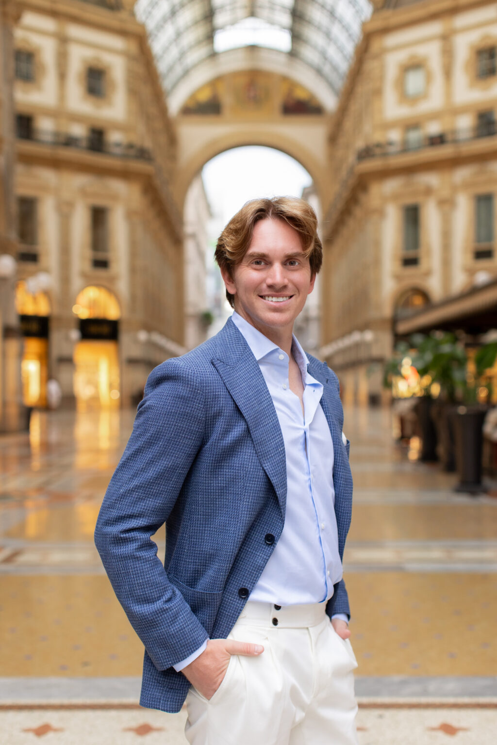A smiling man in a blue jacket posing with hand in pocket in the Galleria Vittorio Emanuele II in Milan.
