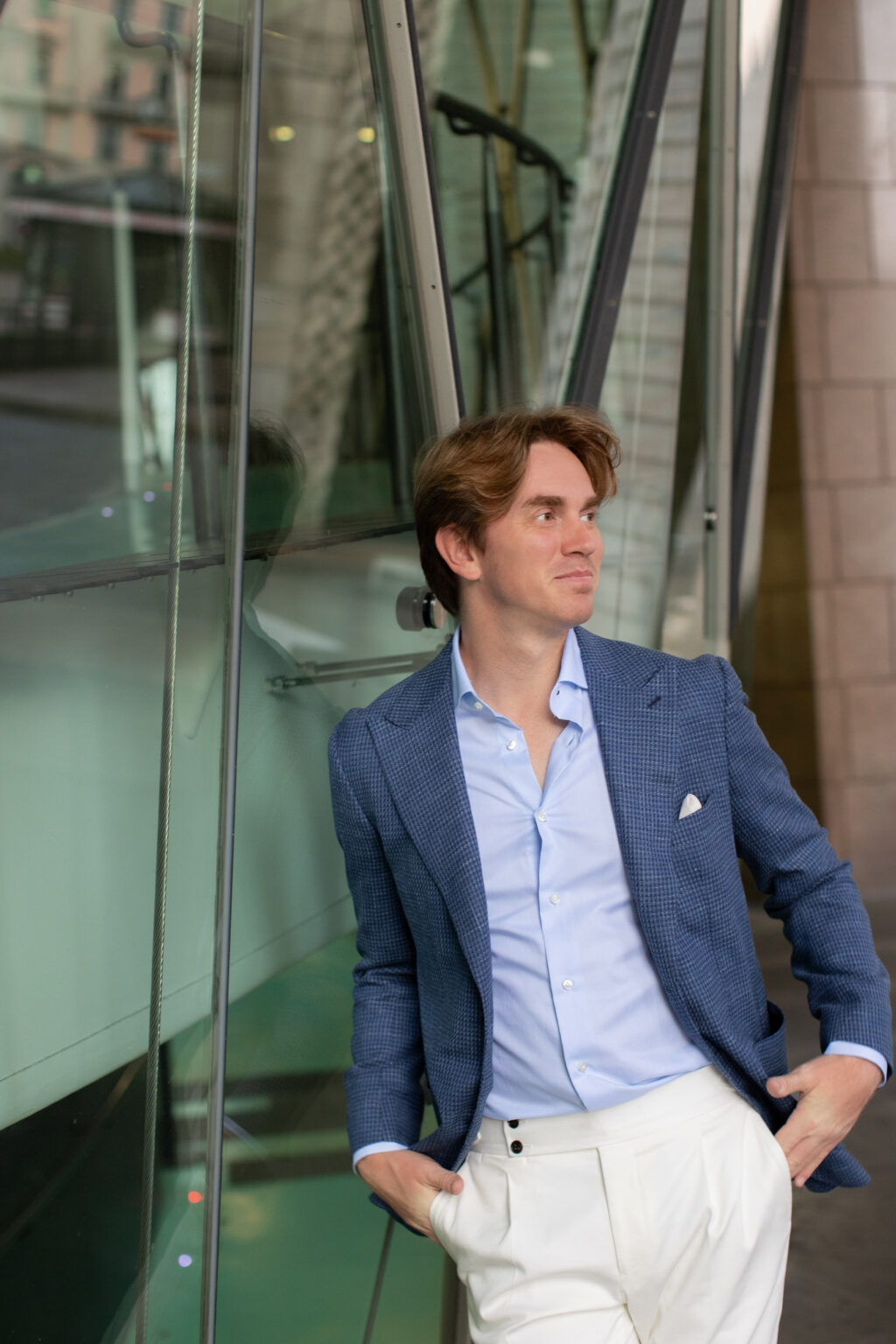 A man in a blue jacket leaning against green-tinted modern glass architecture in central Milan.