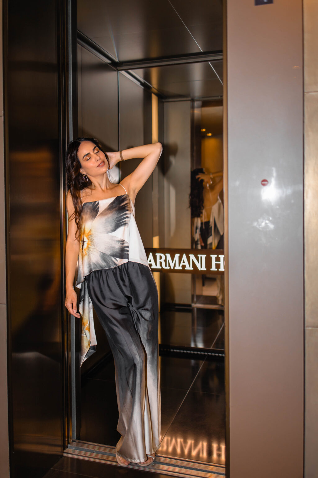 She poses with her eyes closed in a mirrored alcove beside the illuminated Armani Hotel sign inside the Armani Hotel Milano.