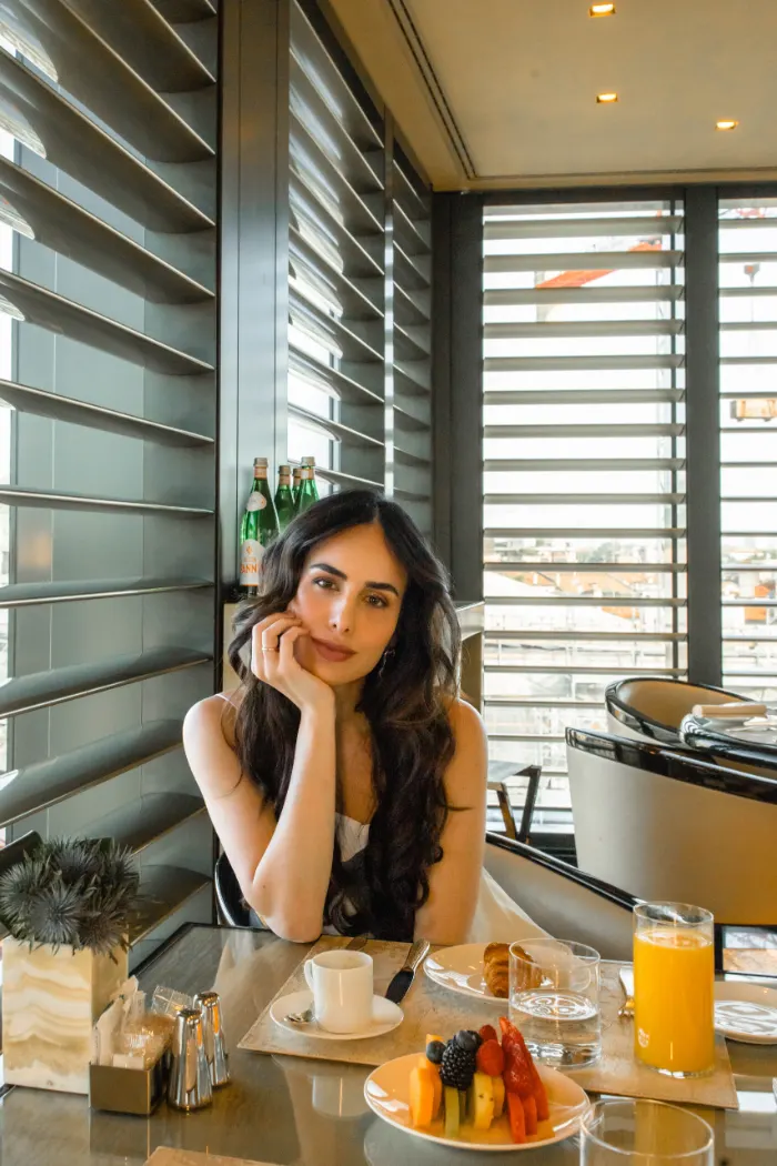 Woman at a hotel breakfast table with espresso and a view over the rooftops of Milan
