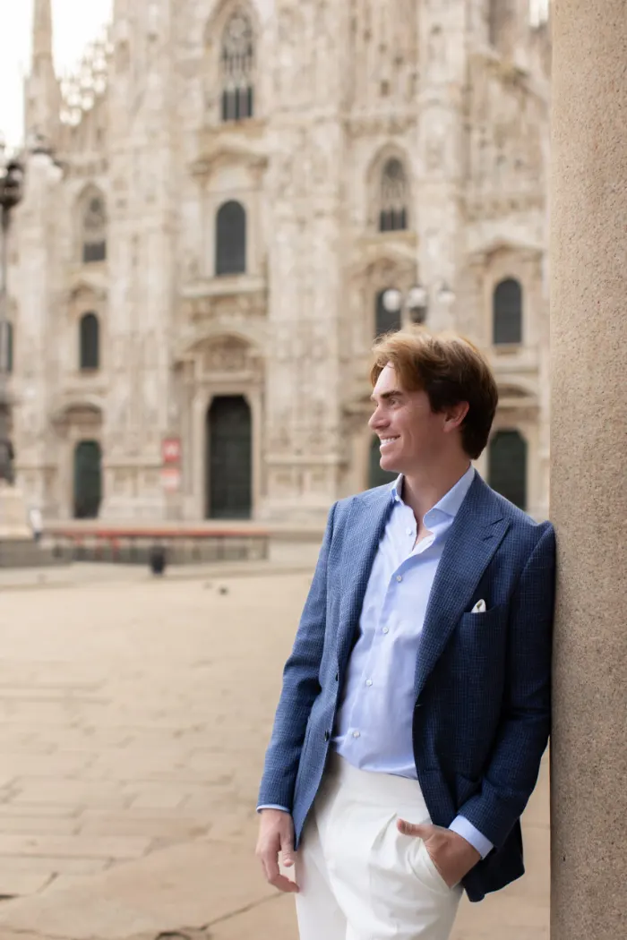 Man in a blue blazer leaning on a stone column by Piazza del Duomo, Milan