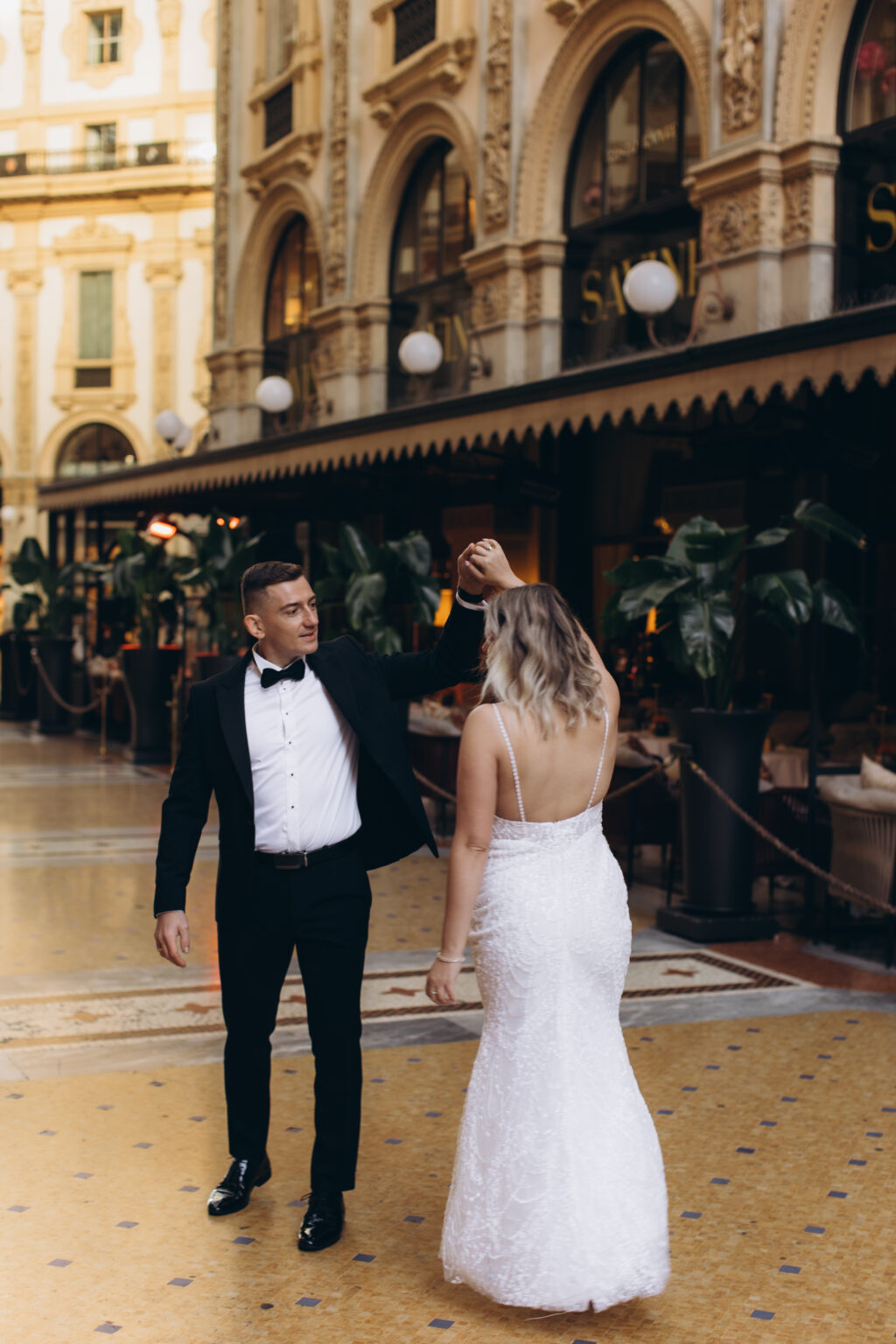 He twirls her in a playful dance on the mosaic floor of the Galleria Vittorio Emanuele II, ornate arcades and café awnings behind them.