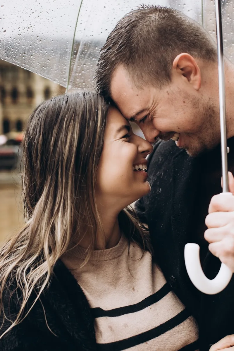 Just engaged couple laughing nose to nose under a clear umbrella in the Milan rain