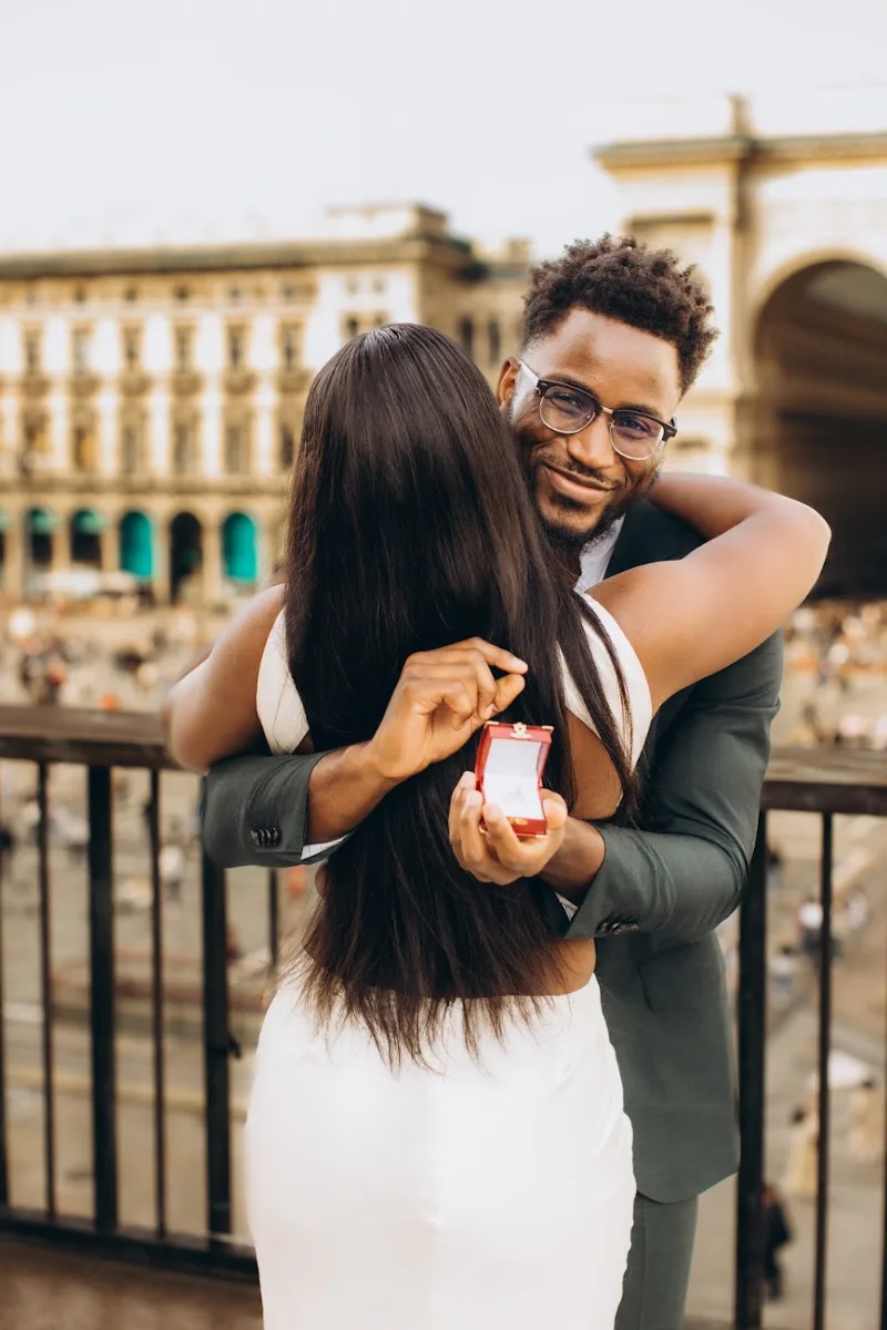 She hugs him as he holds the open ring box on a terrace in central Milan