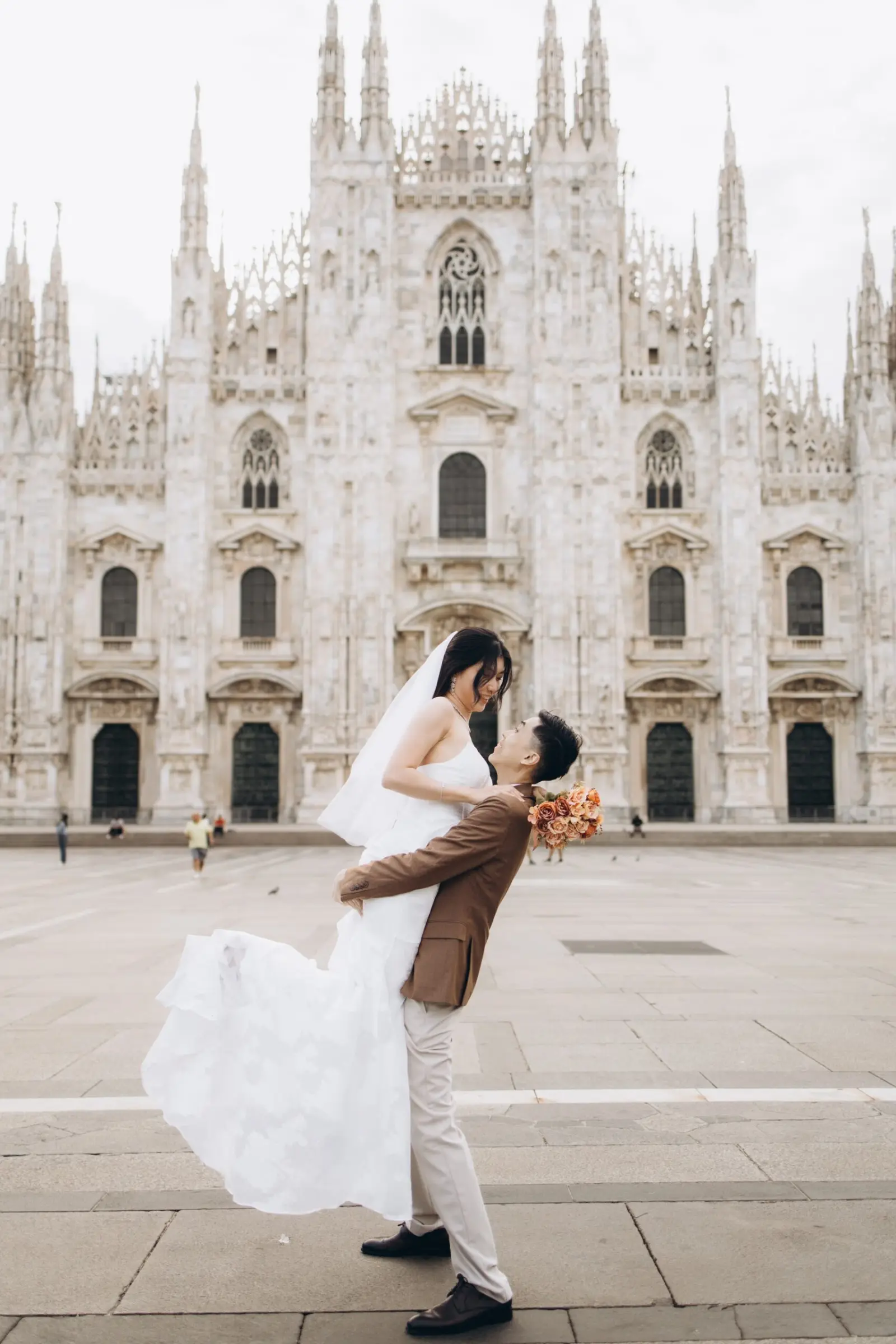 Groom carrying his bride with a bouquet in front of the Duomo in Milan
