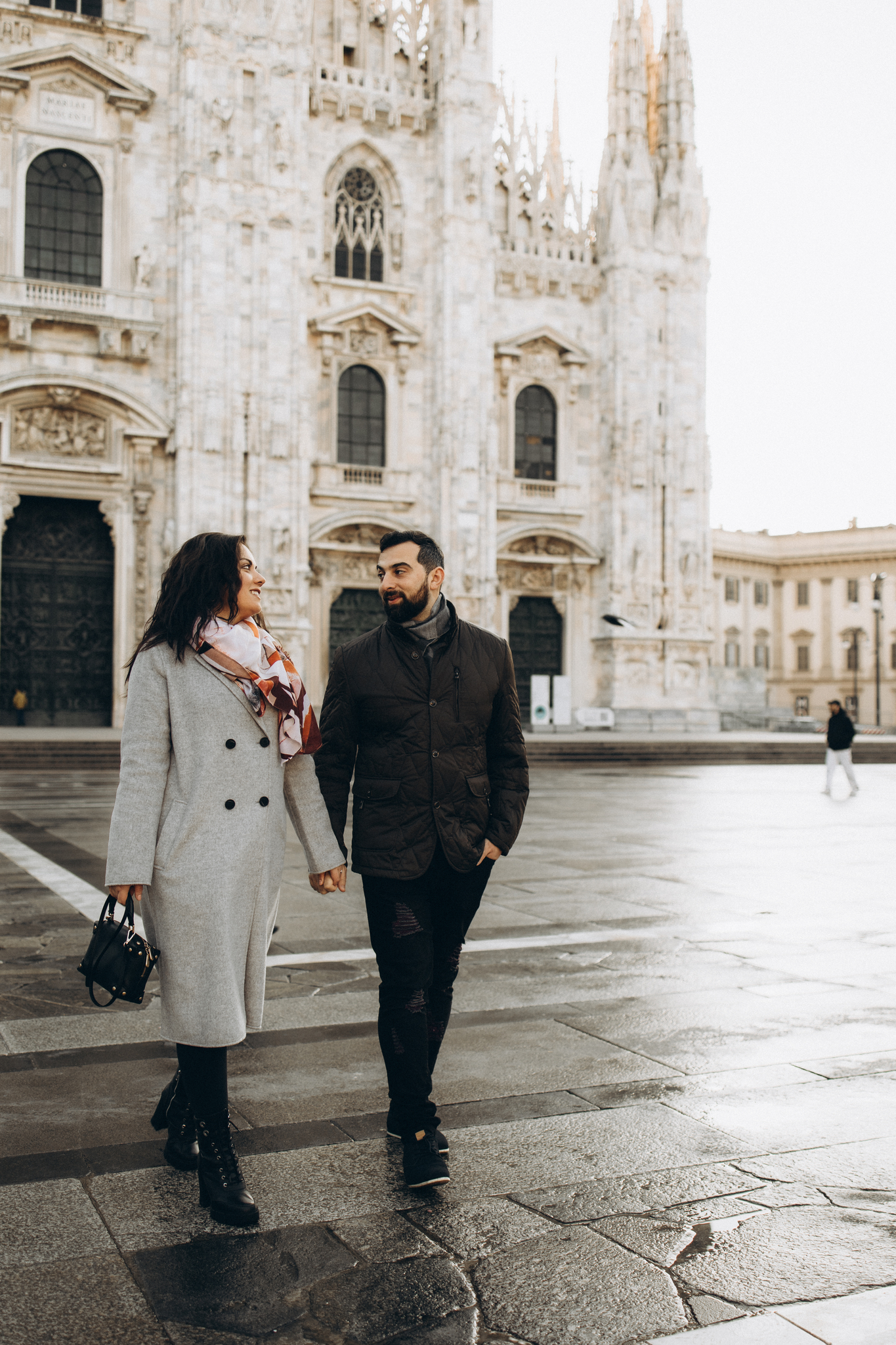 Overcast Winter Walk at Piazza del Duomo, Milan A couple in winter coats walks hand in hand across Piazza del Duomo on an overcast day with the cathedral behind them in Milan