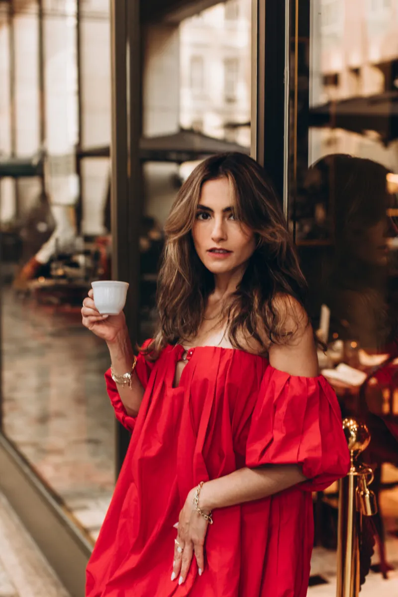 Woman in a red off-shoulder dress with an espresso by a café window in Milan