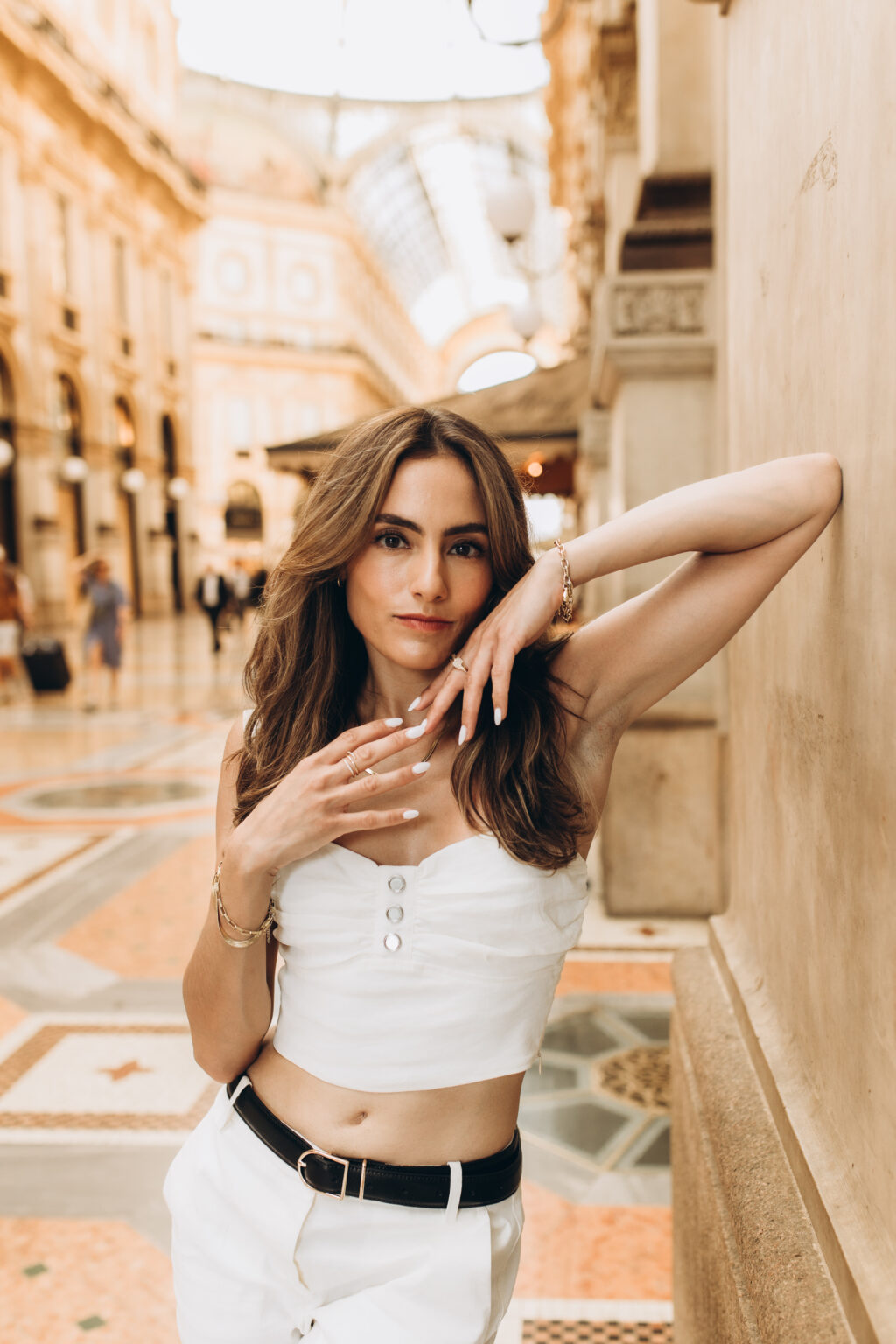 Woman in a white crop top and belt leans against a wall inside the Galleria Vittorio Emanuele II in Milan.