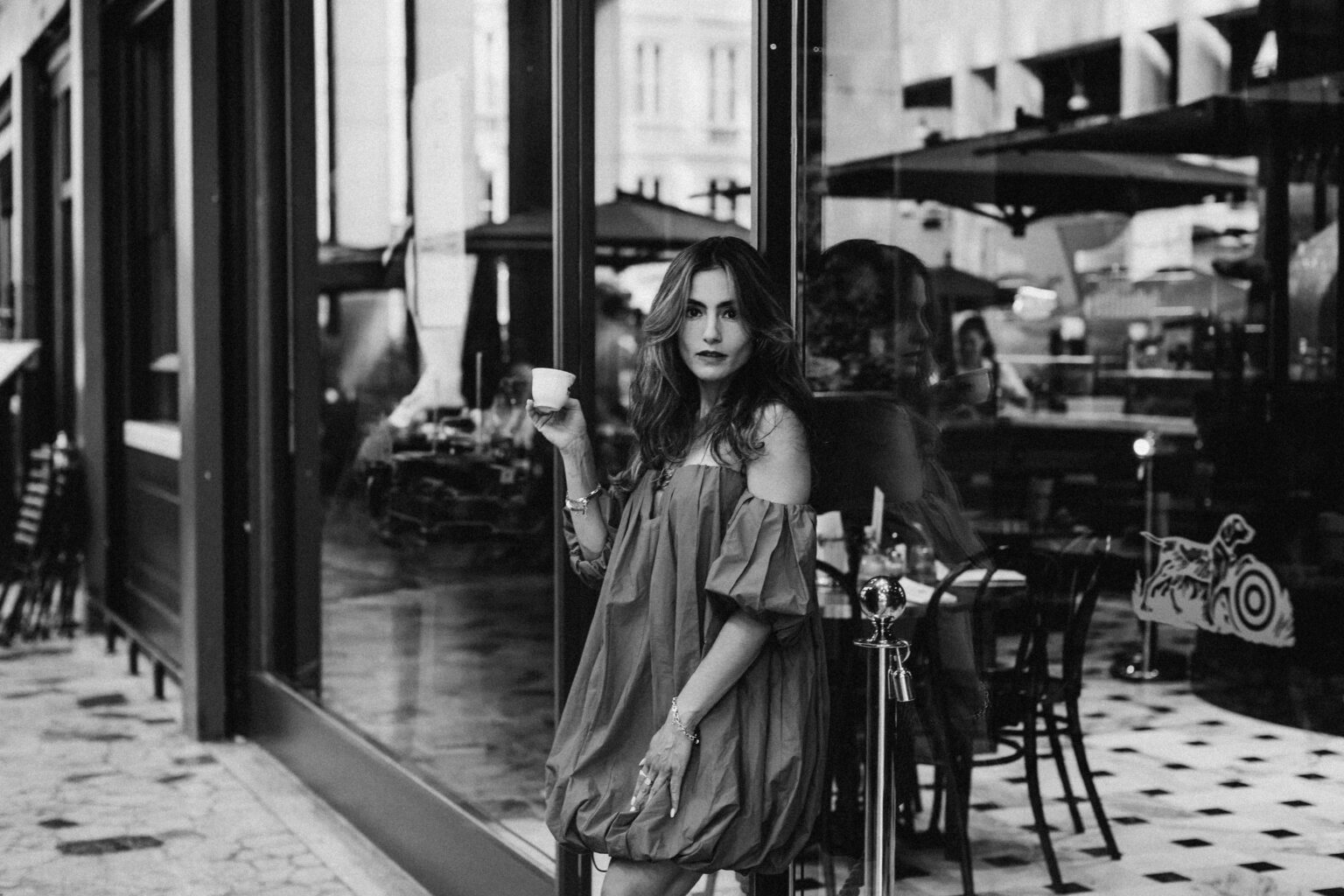 Black and white photo of a woman in a red off-shoulder dress holding an espresso cup by a Milan café.